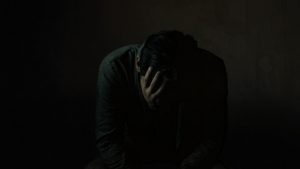 How Much Adderall Is Too Much hero image of a man holding his head while sitting in the dark.